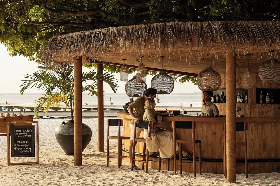 Strandbar under stråtag med trædisk og høje stole på Sun Siyam Iru Fushi