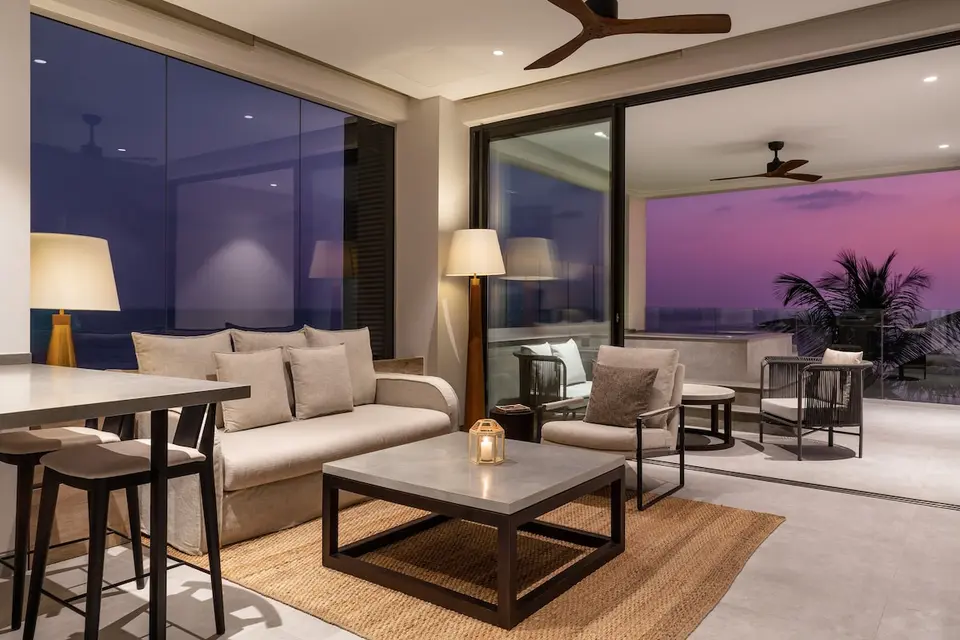 Opholdsrum på Crystal Sands med sofa, lænestol og åben forbindelse til en møbleret balkon i aftenlys.