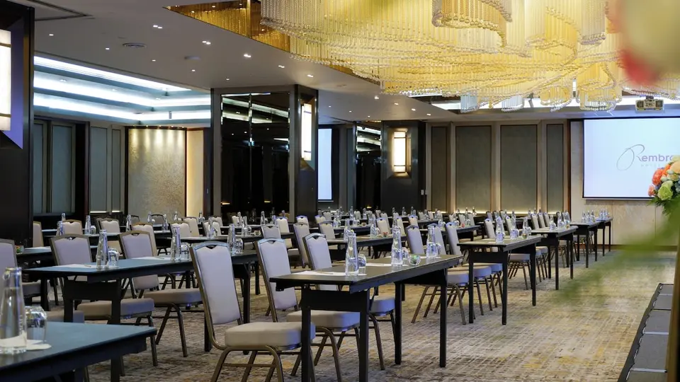 Mødelokale med bordrækker, stole og stor loftsbelysning på Rembrandt Hotel Bangkok.