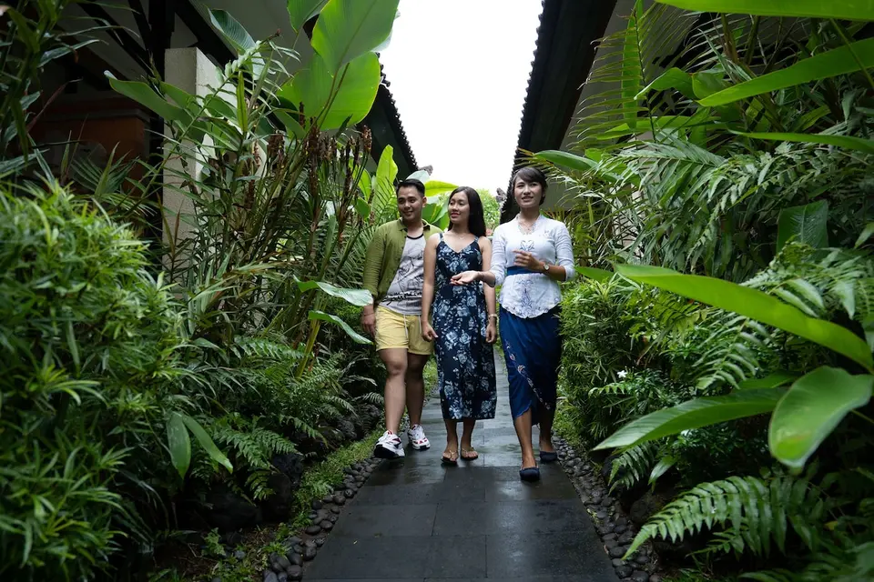 Gæster og medarbejder på en grøn havesti mellem bygninger på Natya Hotel Tanah Lot