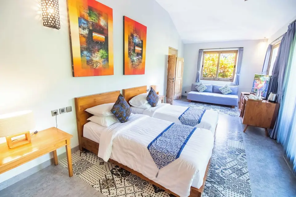 Værelse med to senge, blå sofa og mønstret gulv på Natya Hotel Tanah Lot