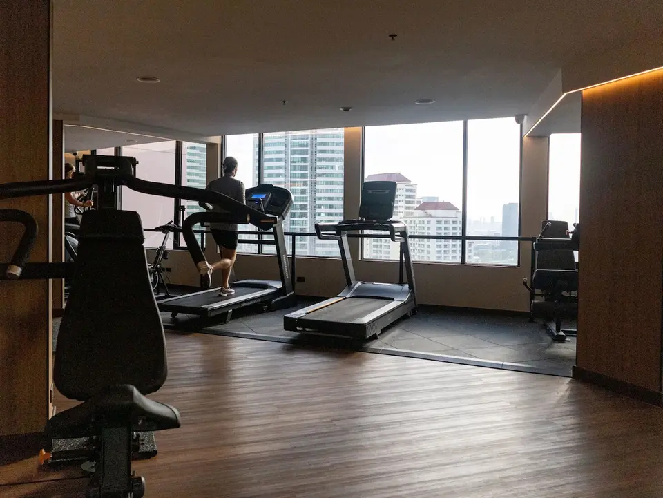 Fitnessrum med løbebånd og store vinduer mod Bangkok på Rembrandt Hotel.