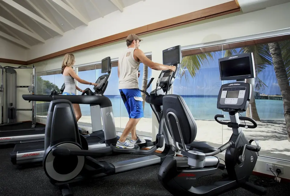 Fitnessrum med gæster på træningsmaskiner og udsigt til lagunen på Centara Ras Fushi
