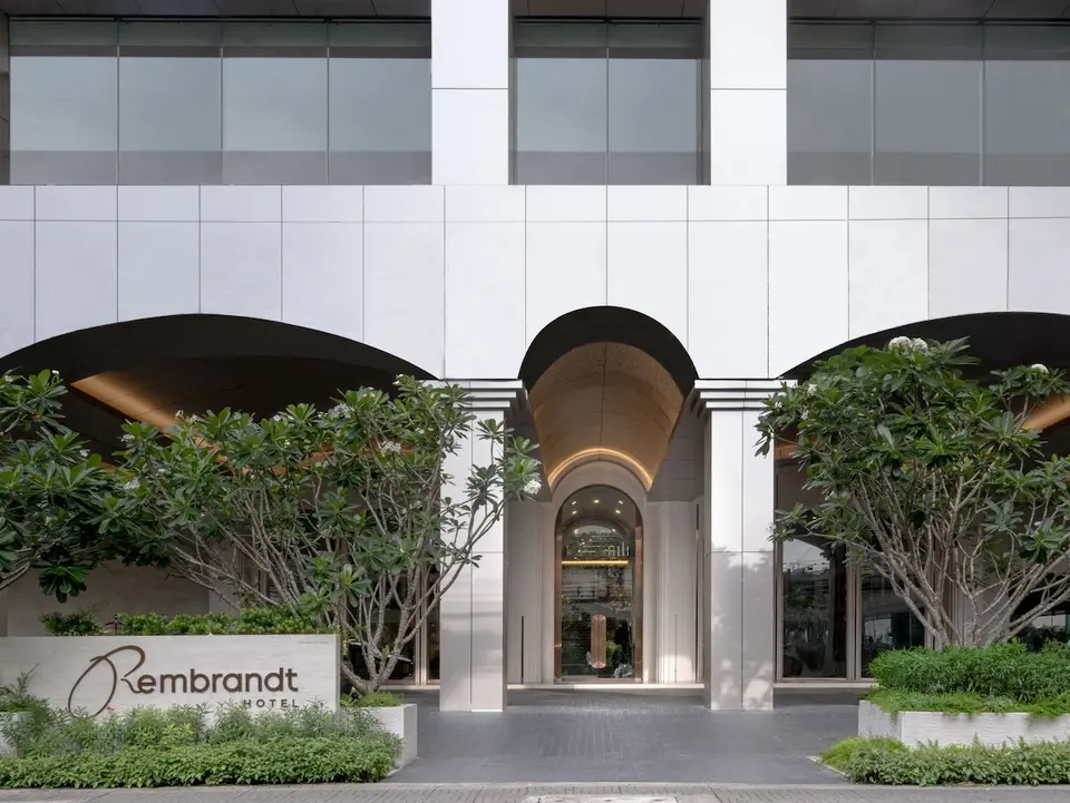 Indgang til Rembrandt Hotel Bangkok med buet portal, hotelskilt og grøn beplantning.