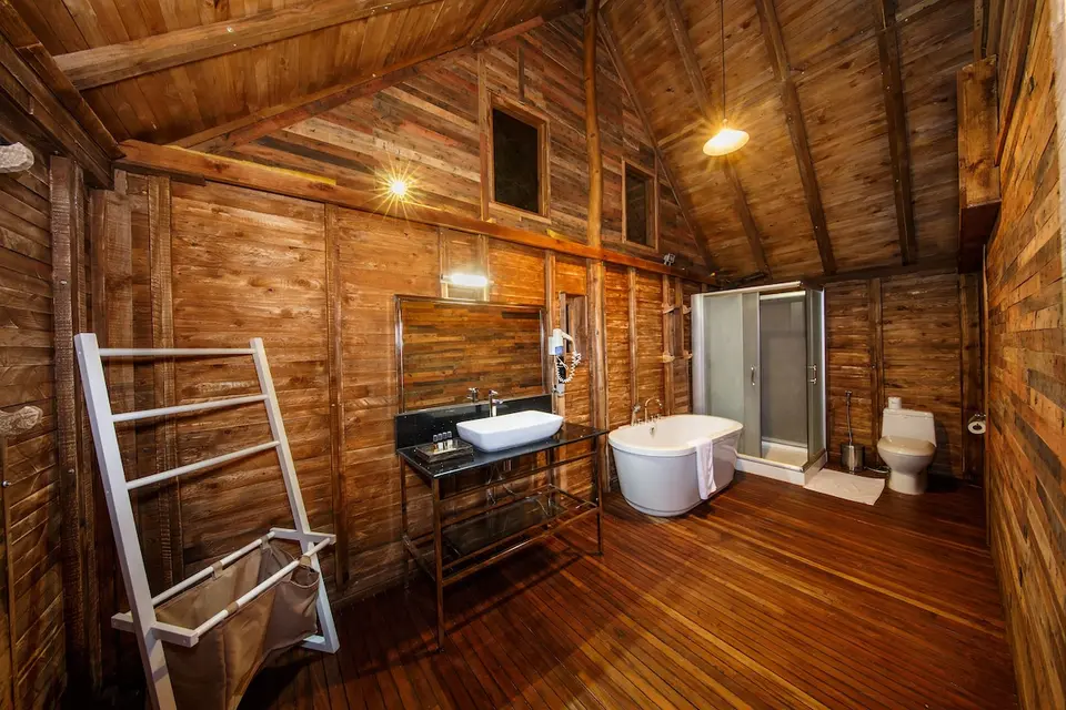 Badeværelse i en træchalet på Aliya Resort med fritstående badekar, håndvask og brusekabine.