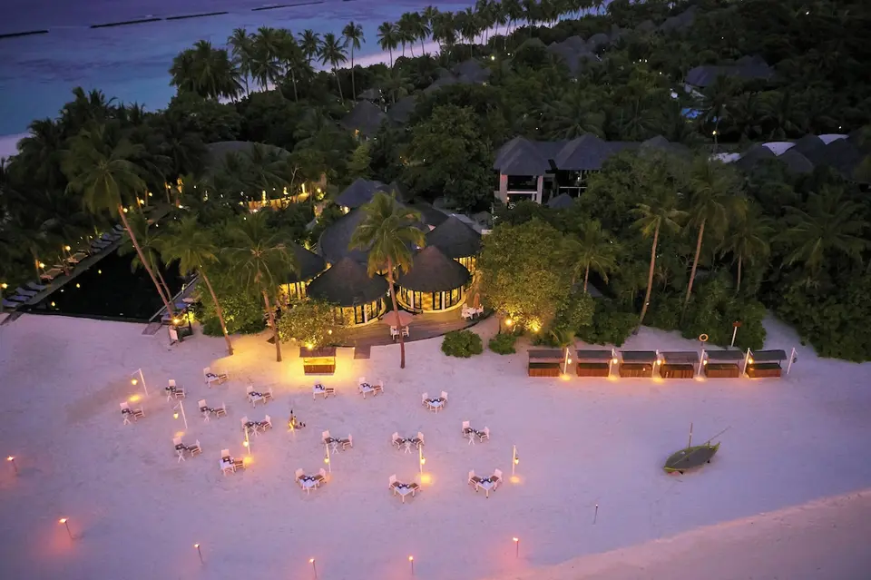 Borde på stranden og oplyste bygninger i skumringen på Sun Siyam Iru Fushi