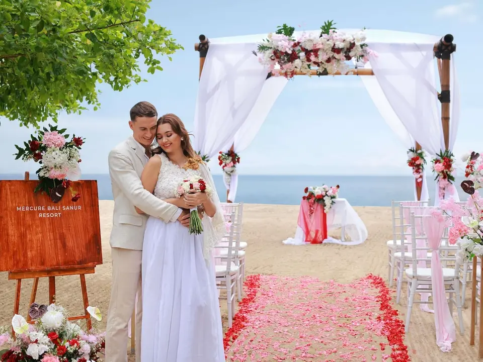 Brudepar ved blomsterbue på stranden foran Mercure Resort Sanur