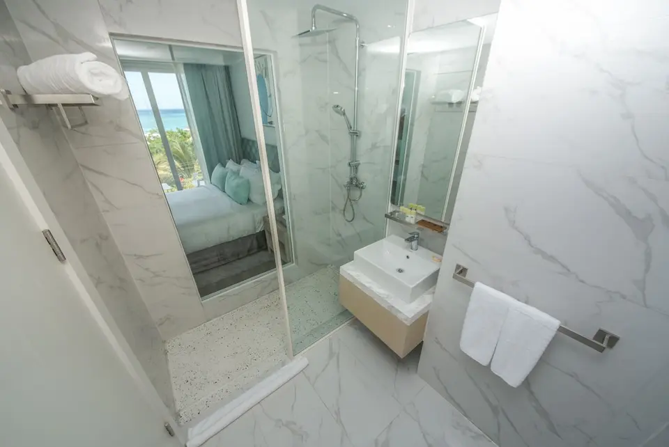 Lyst badeværelse med glasbruser, håndvask og spejl på Ocean V Hotel
