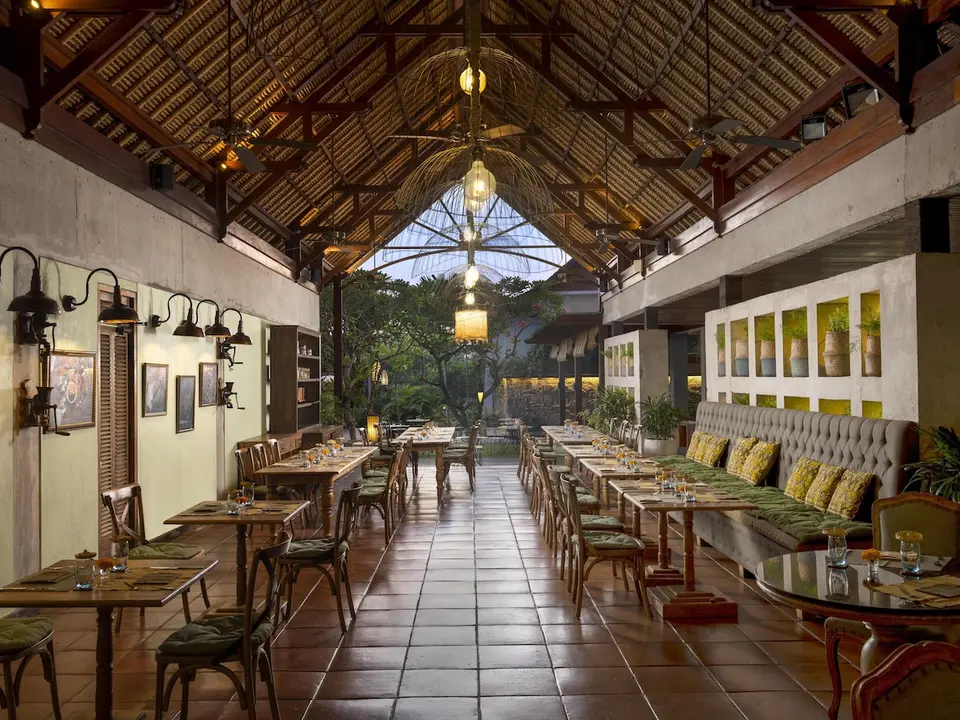 Restaurant med højt trætag, lange rækker af borde og en polstret bænk langs væggen.