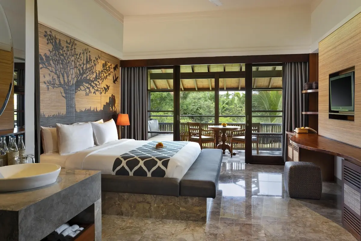 Værelse med dobbeltseng, vægdekoration med træmotiv og møbleret balkon på Alaya Resort Ubud.