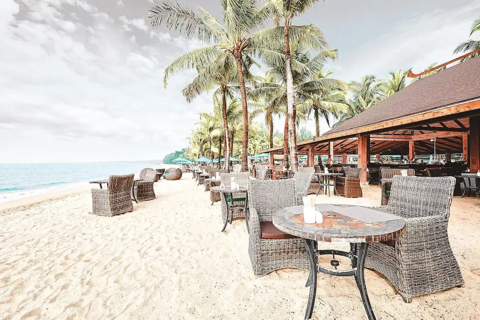Restaurantborde og flettede stole på sandet ved havet.