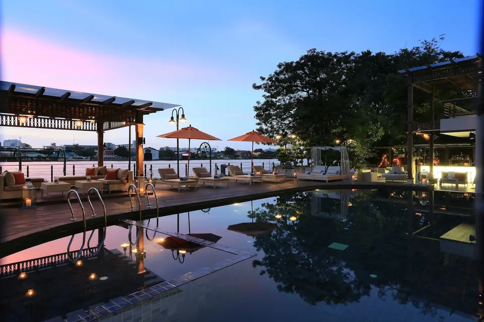Poolterrasse med liggestole og udsigt over floden ved skumring.