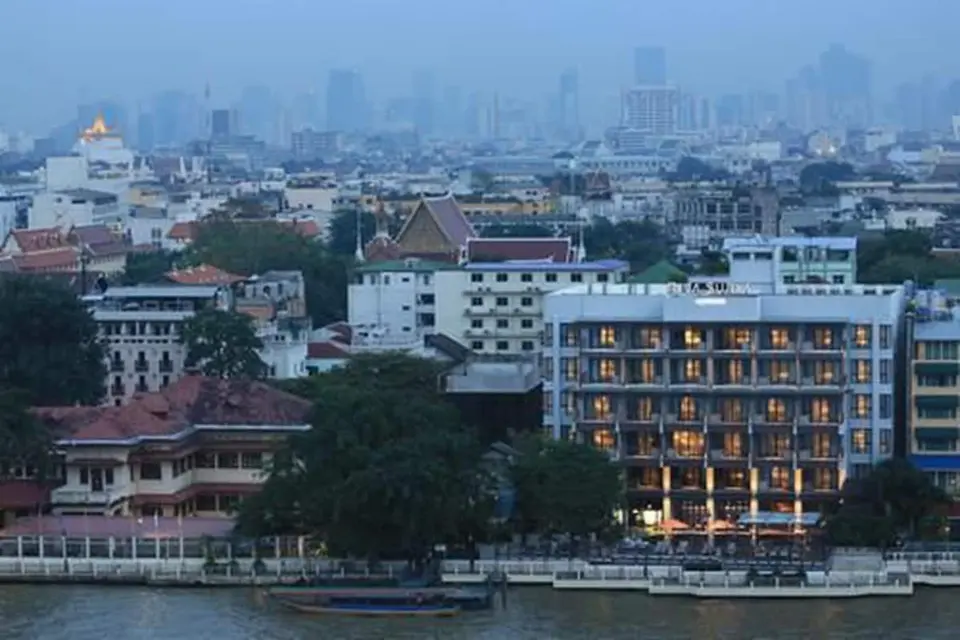 Riva Surya Bangkok set fra flodsiden med byens bygninger i baggrunden.