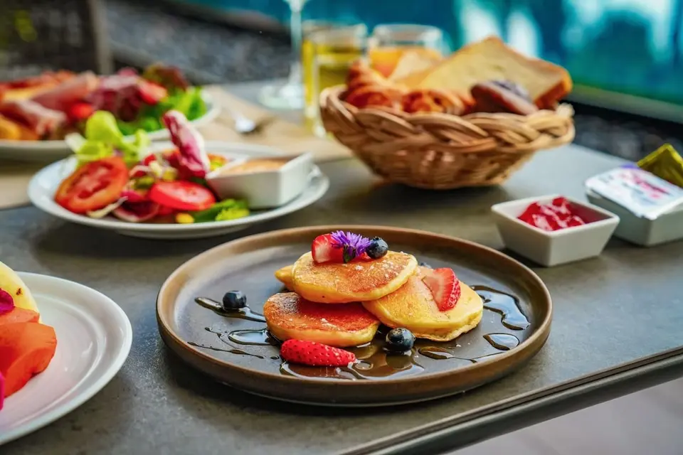 Morgenmadsbord med pandekager, bær, brød og salat.
