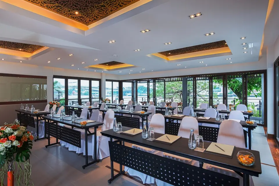 Mødelokale med bordrækker og store vinduer på Riva Surya Bangkok.
