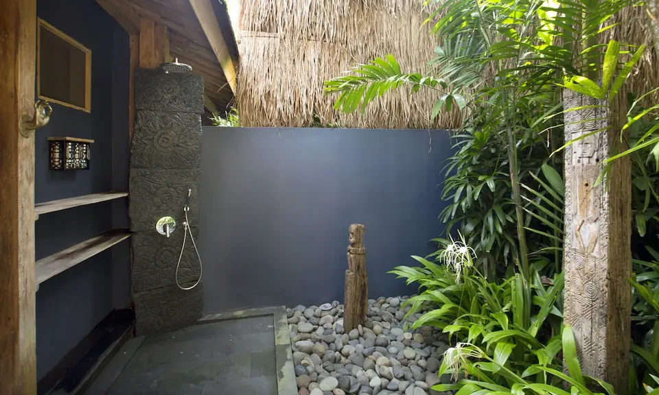 Delvist udendørs bruser med planter og stenvæg på Blue Karma Dijiwa Ubud.