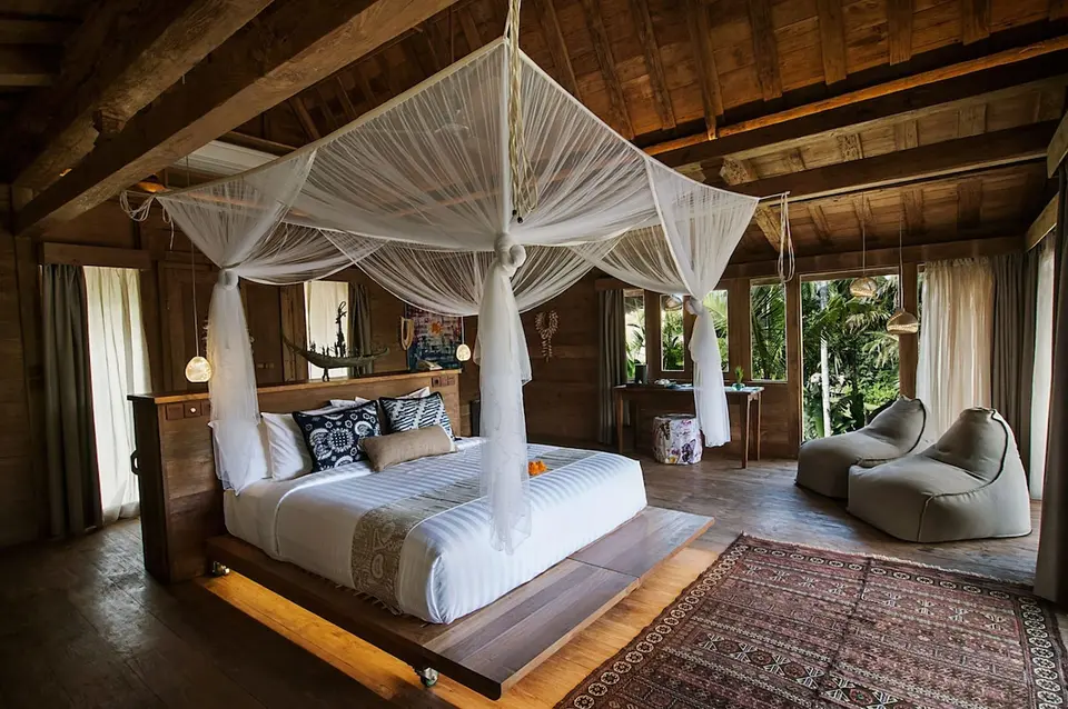 Værelse med himmelseng og lænestole i træindretning på Blue Karma Dijiwa Ubud.