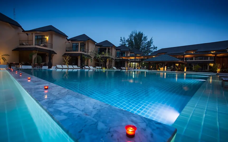 Oplyst pool med liggestole og hotelbygninger i skumringen.