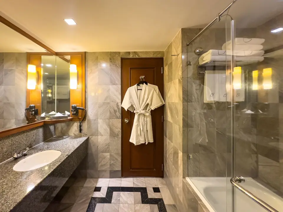 Badeværelse med badekar, glasafskærmning og stor håndvask på Rembrandt Hotel Bangkok.