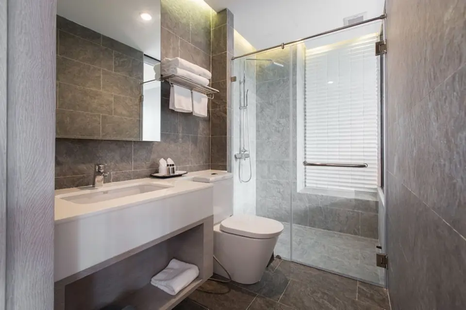 Badeværelse med håndvask, toilet og glasafskærmet bruseniche