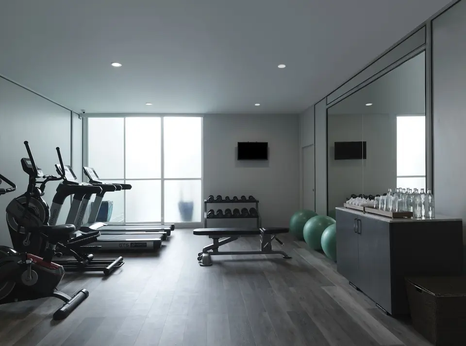 Fitnessrum med løbebånd, motionscykel, håndvægte og spejlvæg.