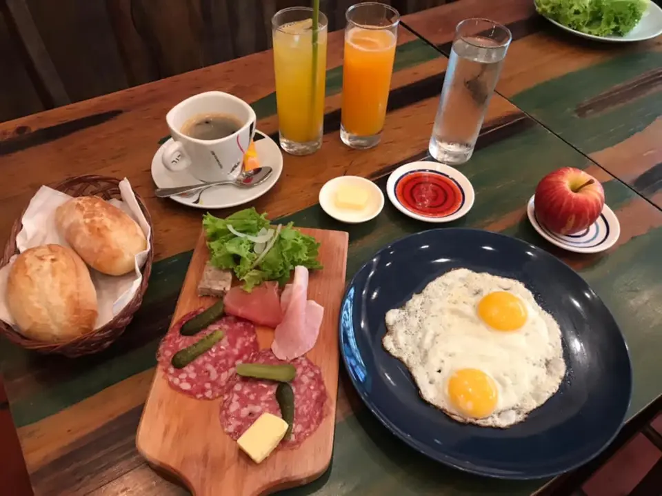 Morgenmad med spejlæg, brød, pålæg, kaffe og juice på et træbord.