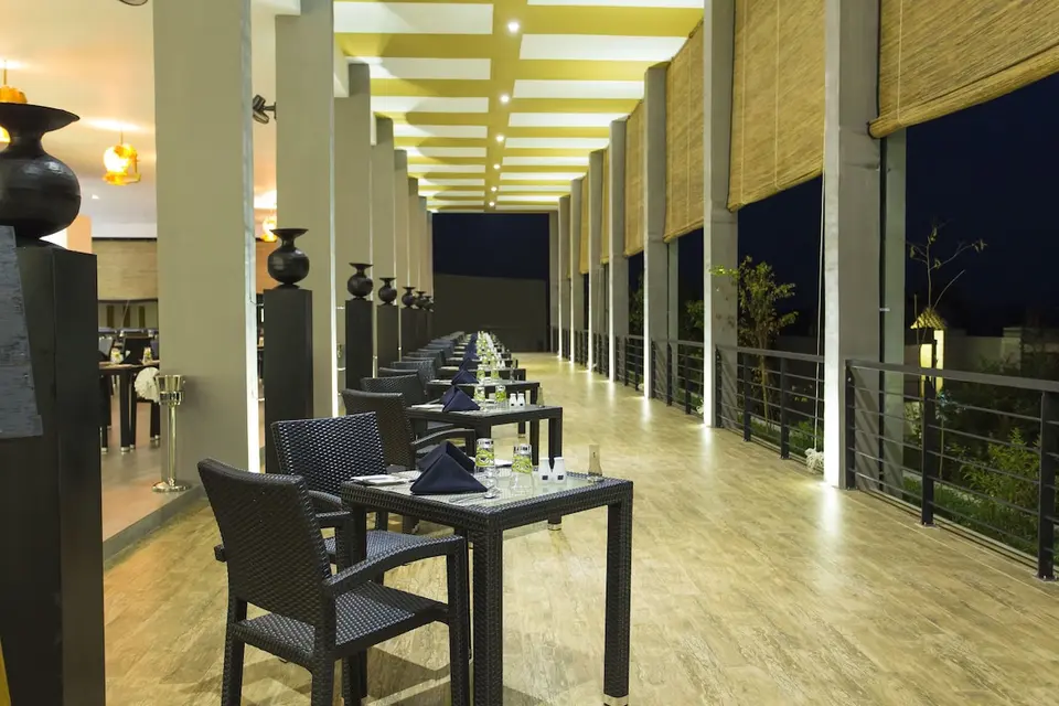 Dækkede borde langs restaurantens åbne side på Aliya Resort i aftenbelysning.