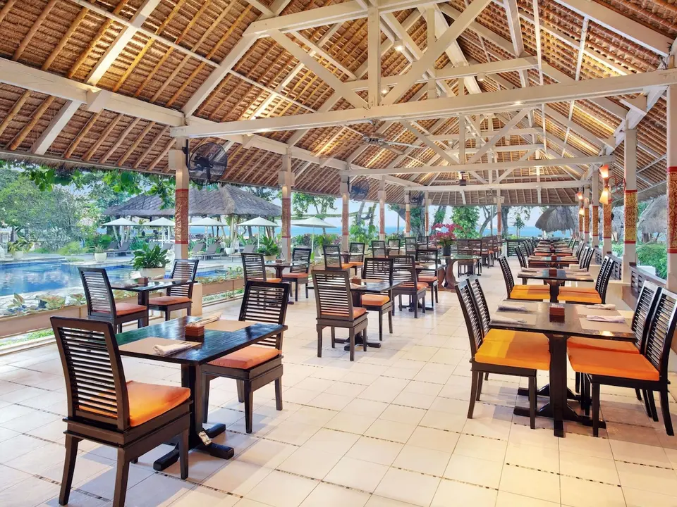 Åben restaurant med borde under stråtag ved poolen på Mercure Resort Sanur