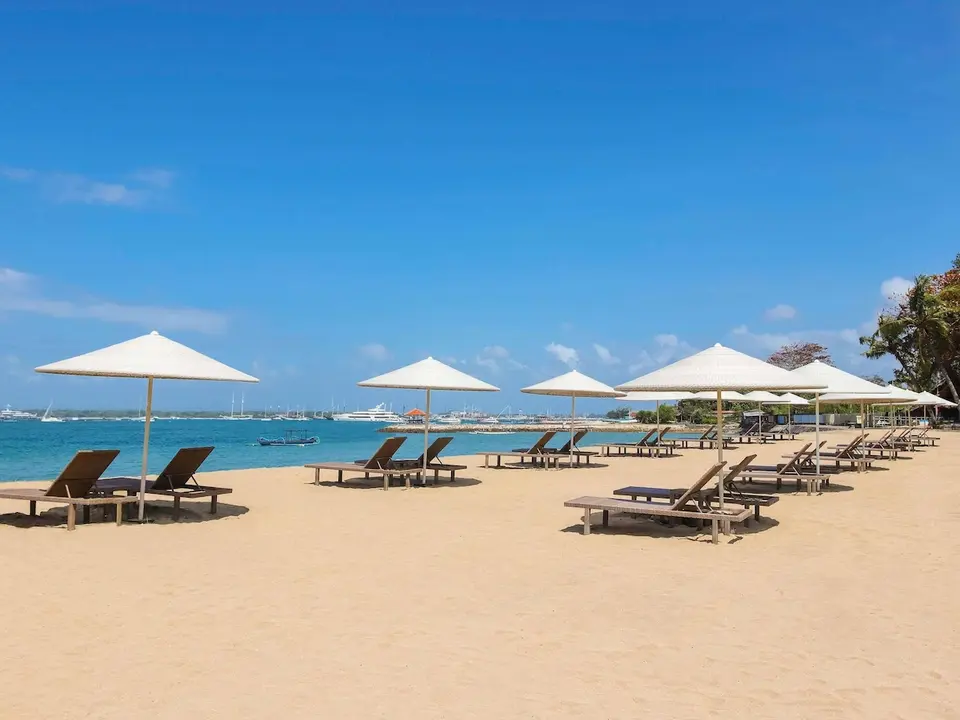 Liggestole og hvide parasoller på stranden ved Mercure Resort Sanur