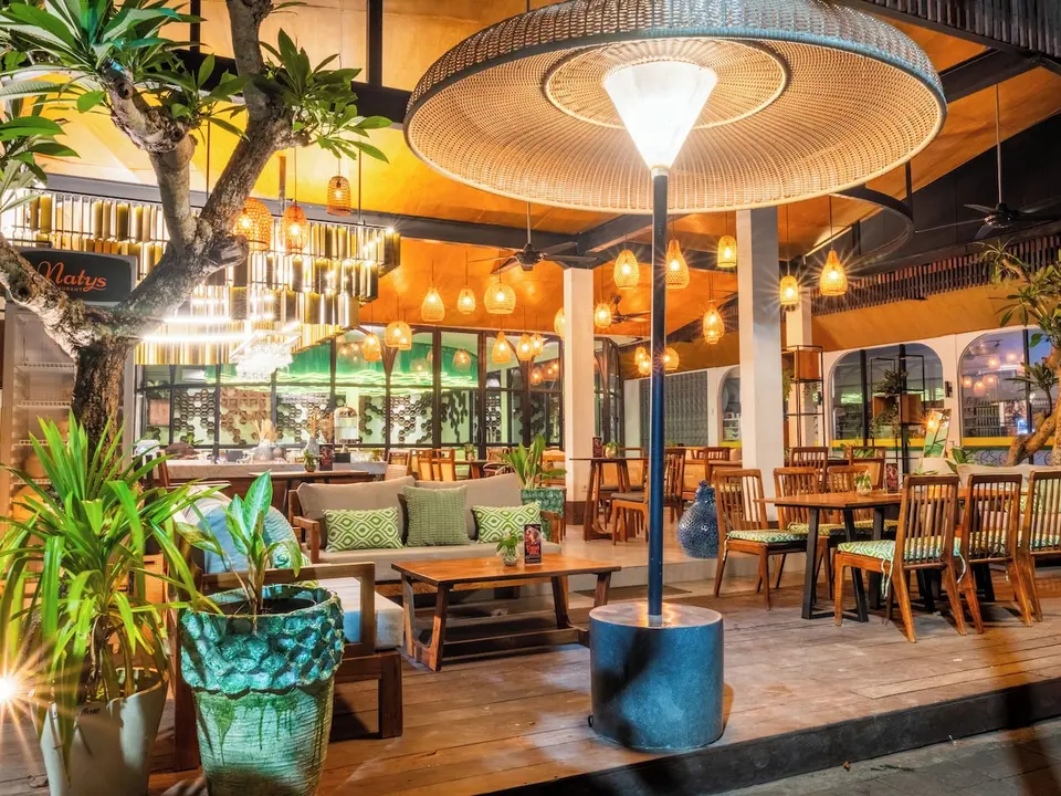 Restaurant med træmøbler, grønne planter og hængende lamper på Natya Hotel Tanah Lot