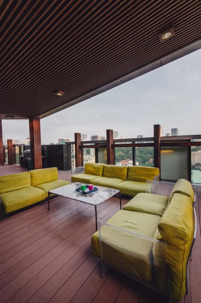 Overdækket terrasse med grønne sofaer og udsigt over byens tage.