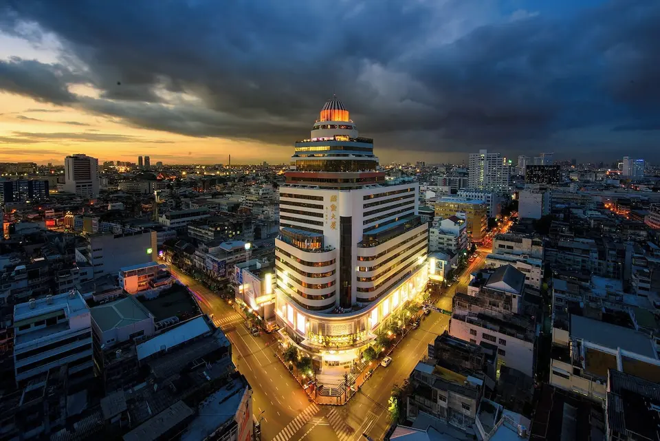 Grand China Bangkok med oplyst facade og byens gader omkring hotellet i skumringen.