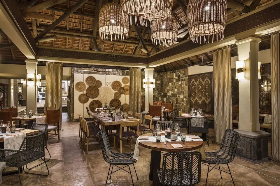 Restaurant med dækkede borde, flettede stole og store kurvelamper under stråtag på Heritage Awali
