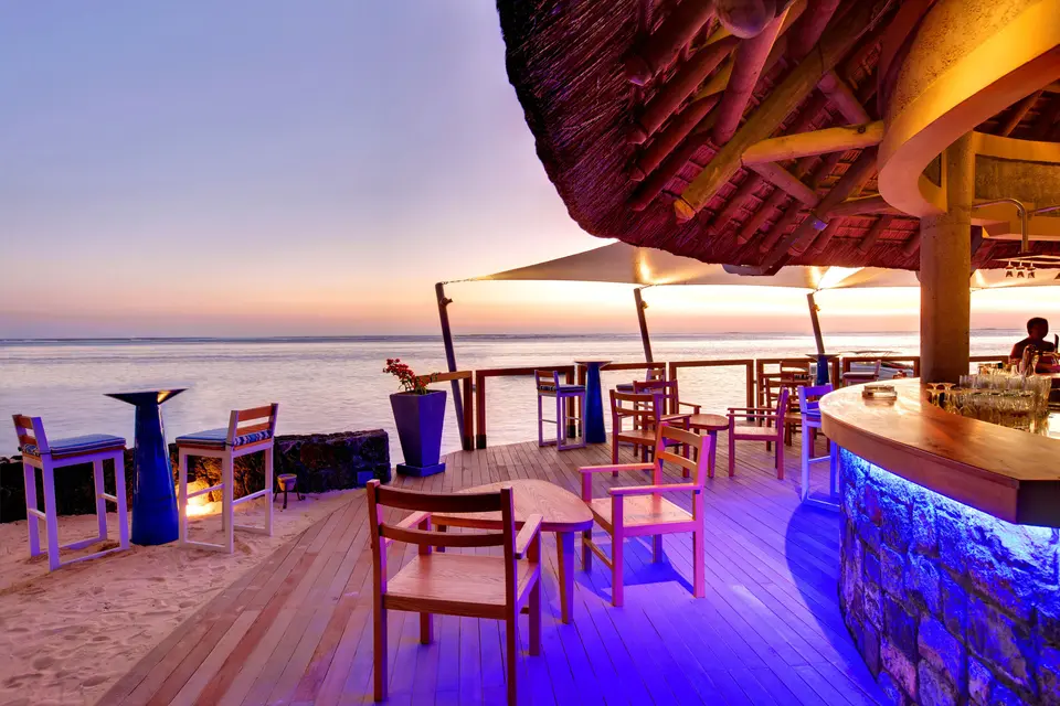 Belyst strandbar på Heritage Awali med høje stole og havudsigt ved solnedgang