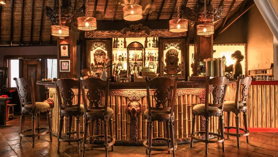 Bar på Hotel Tugu Bali med udskårne træstole, bambusfront og hængelamper.