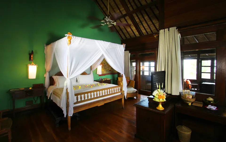 Værelse på Hotel Tugu Bali med himmelseng, skrivebord og grøn væg.