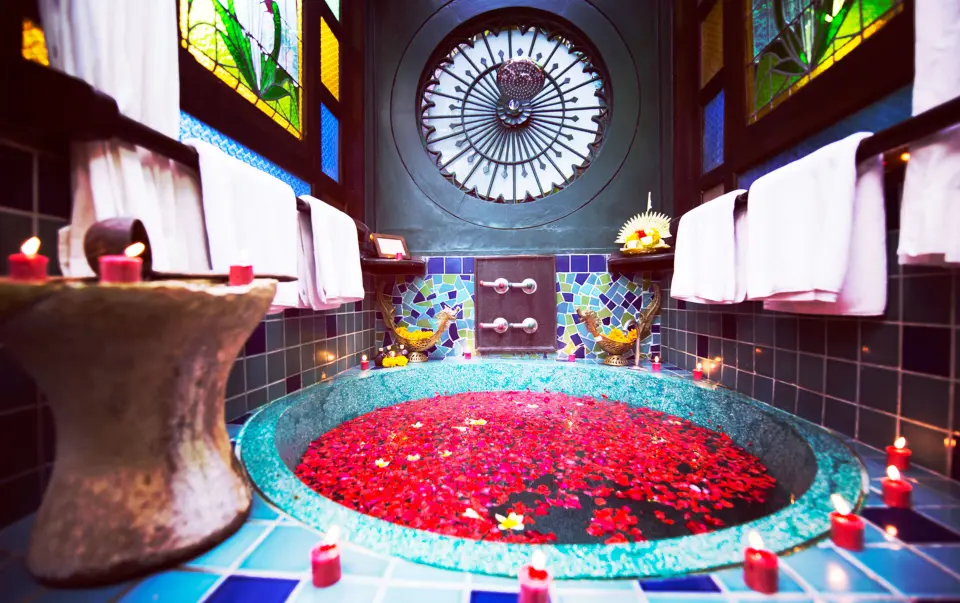 Rundt mosaikbad med blomsterblade, stearinlys og farvede glasvinduer på Hotel Tugu Bali.