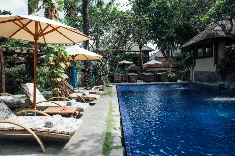 Pool på Hotel Tugu Bali med liggestole, parasoller og tropiske planter.