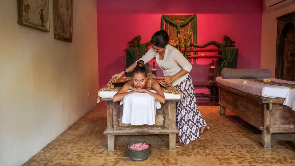Massage i Hotel Tugu Balis spa med udskårne træbrikse og røde vægge.