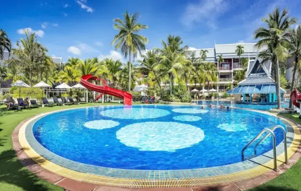 Udendørs pool med rød vandrutsjebane, palmer og liggestole ved Chada Thai Village.