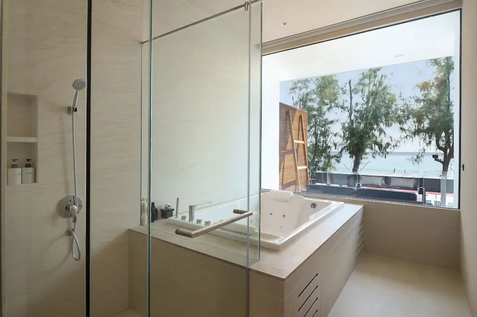 Badeværelse med glasbruser, badekar og vindue mod havet på Idyllic Concept Resort.