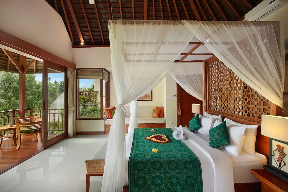 Værelse med højt træloft, himmelseng og møbleret balkon på Jannata Resort & Spa.