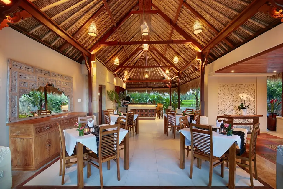 Restaurant med højt træloft og opdækkede borde på Jannata Resort & Spa.