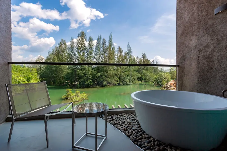 Badekar og stol på en balkon med udsigt til vand og træer ved Kalima Khao Lak