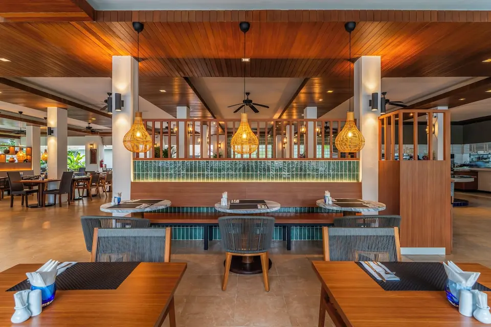 Restaurant med træloft, fletlamper og dækkede borde på Sunprime Kamala Beach.