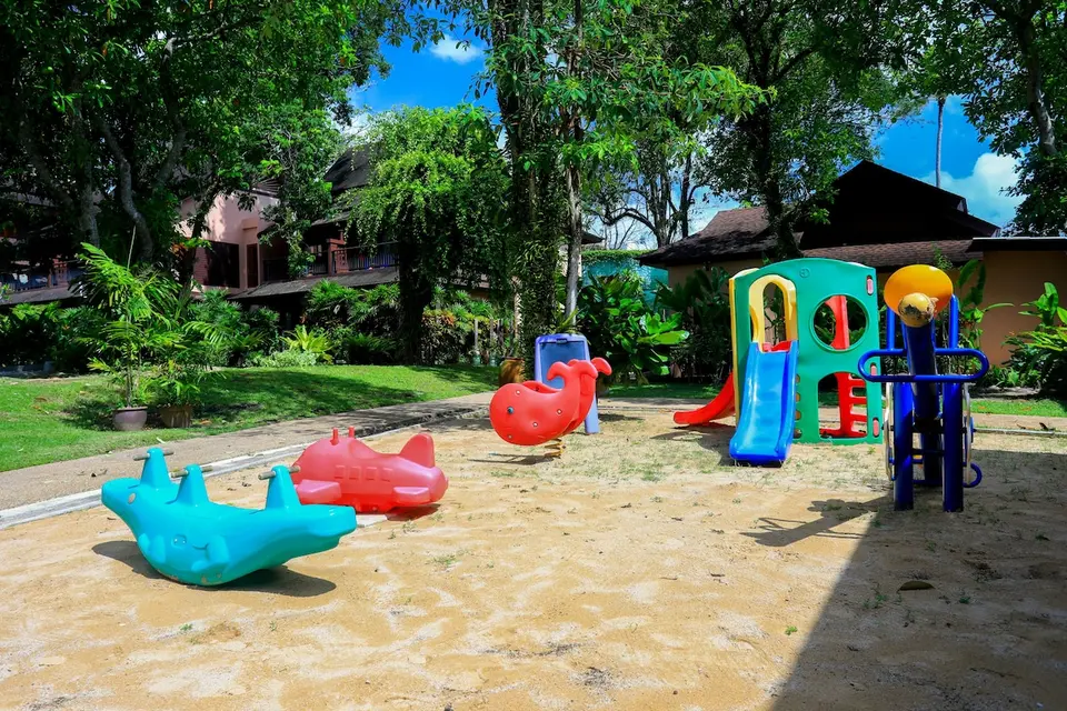 Legeplads på Khaolak Merlin Resort med små rutsjebaner og vippedyr på sand mellem grønne træer