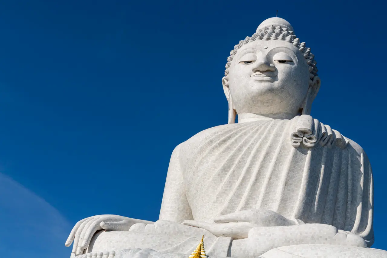 En stor hvid Buddha-statue set nedefra mod en blå himmel.