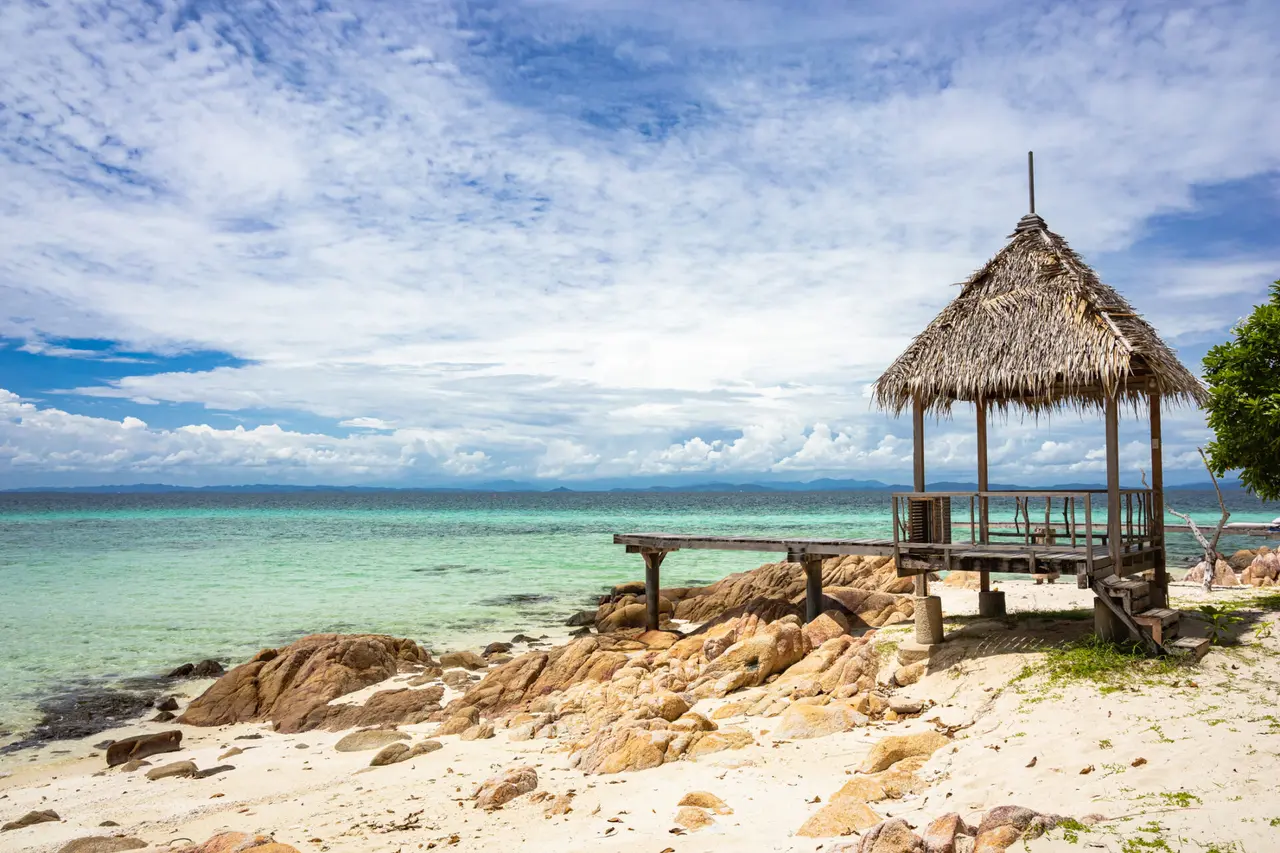Pavillon med stråtag ved klipper og klart vand på Koh Munnork