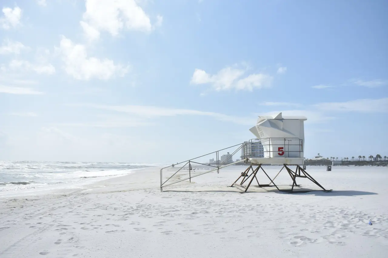 Et hvidt livreddertårn med tallet 5 på en bred sandstrand ved havet.