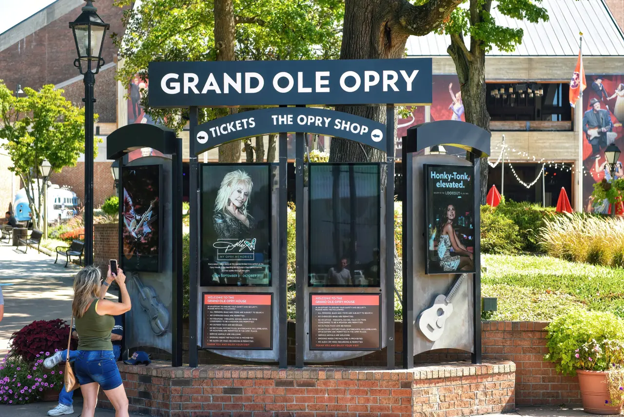Skilt og informationstavler ved Grand Ole Opry med en besøgende foran.